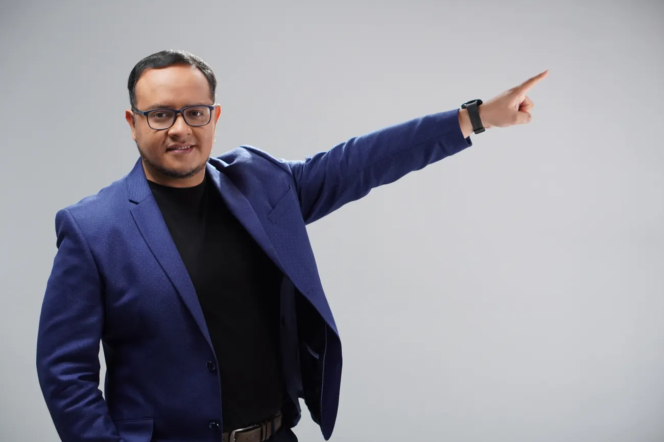 Fernando Angulo, studio portrait in blue blazer, gesturing to one side