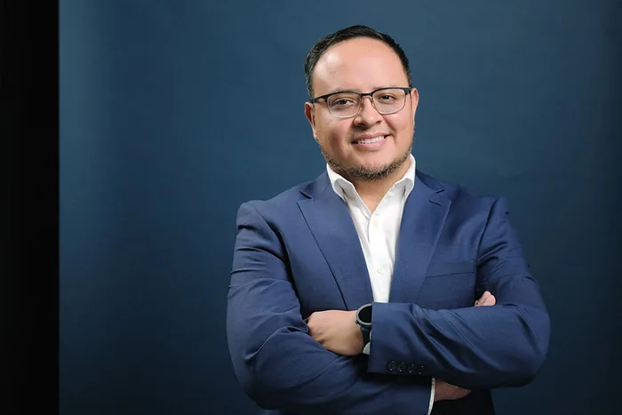 Fernando Angulo sonriendo, brazos cruzados, recorte horizontal, fondo de estudio azul marino