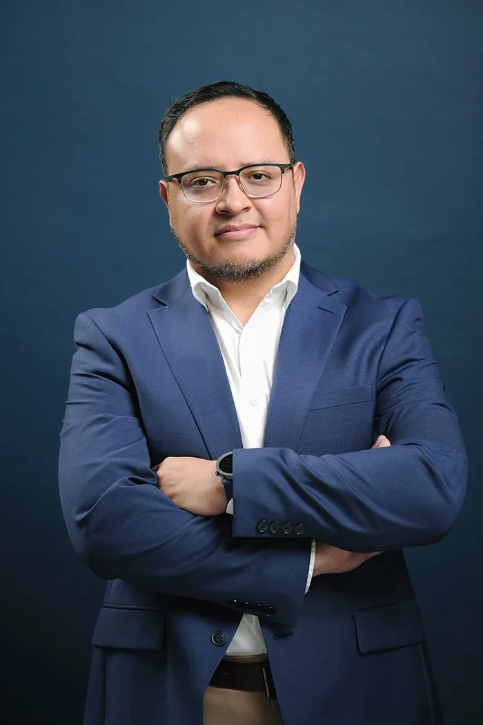 Fernando Angulo, expresión segura, brazos cruzados, fondo de estudio azul marino