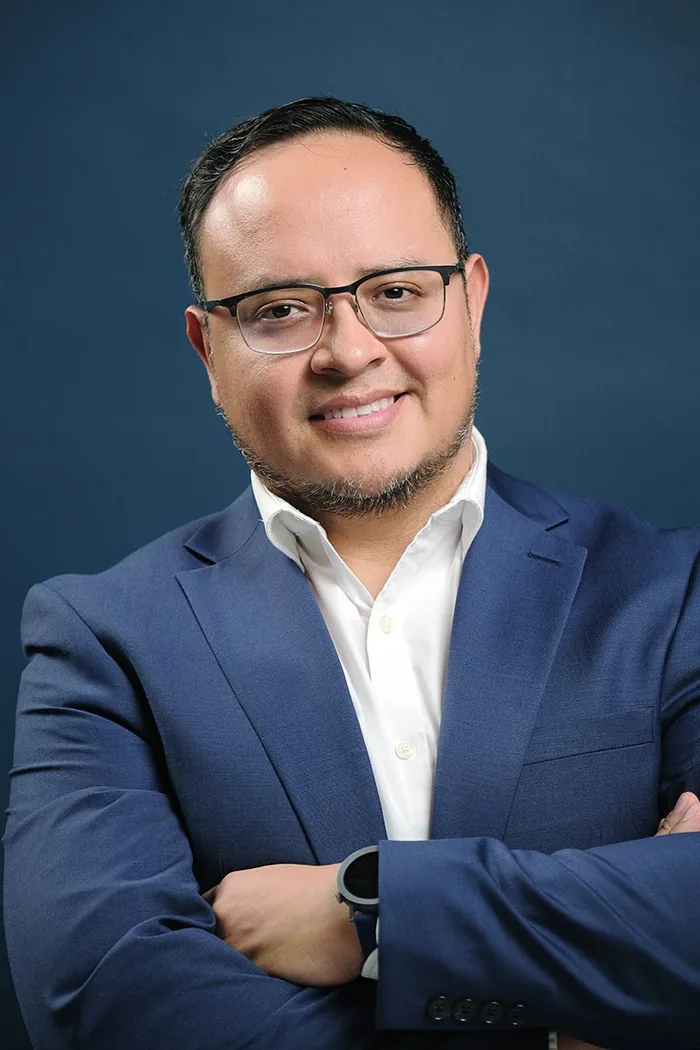 Fernando Angulo sonriendo, brazos cruzados, fondo de estudio azul marino
