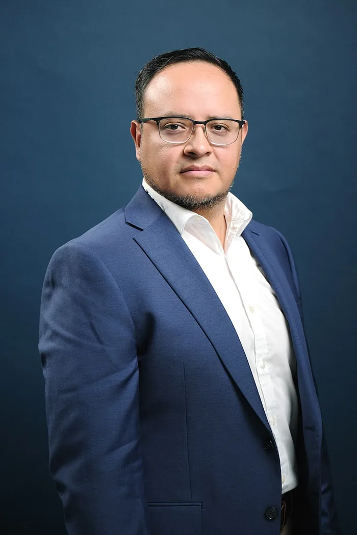 Fernando Angulo de pie, pose de tres cuartos, fondo de estudio azul marino